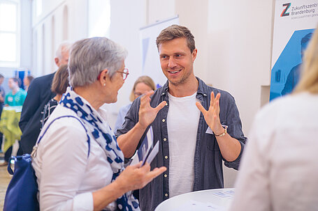 Zwei Personen im lebhaften Gespräch bei einer Veranstaltung, im Hintergrund Zukunftszentrum-Brandenburg-Banner