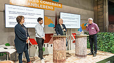Vier Personen auf Bühne bei Podiumsdiskussion, Leitfragen Session 2 auf Bildschirmen, Smart Country Brandenburg