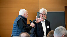 Zwei ältere Männer im Gespräch, einer hält Mikrofon, der andere gestikuliert
