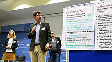 Mann präsentiert mit Mikrofon vor einem Flipchart mit der Aufschrift AG Beteiligung