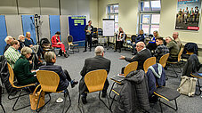 Große Gruppe sitzt im Stuhlkreis bei einem Workshop, eine Person spricht und gestikuliert