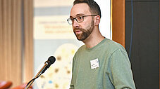 Mann im grünen Pullover spricht am Mikrofon am Rednerpult