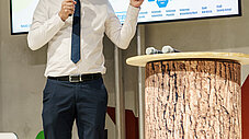 Person präsentiert an einem Podium mit Mikrofon; hinter ihr eine große Leinwand mit einem Netzwerkdiagramm regionaler Projekte