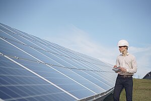 Mann mit Bauhelm steht vor Photovoltaikanlage
