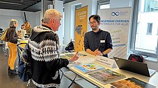 Zwei Personen im Gespräch am Stand der Agentur für Erneuerbare Energien mit Informationsmaterial und Laptop
