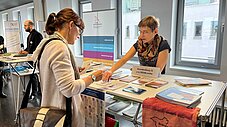 Person am Infostand von Brandenburg 21 e.V./RENN.mitte betrachtet Broschüren, Standbetreuerin steht gegenüber