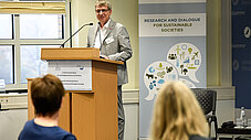 Person spricht an einem Rednerpult vor einem IASS-Banner mit der Aufschrift "Research and Dialogue for Sustainable Societies".