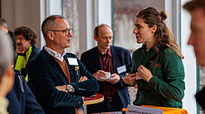 Mann und junge Frau im grünen Jugendforum-Hoodie sprechen am Stand des Jugendforums Nachhaltigkeit