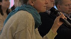Person im Publikum hält Mikrofon und spricht, weitere Zuhörende sitzen daneben