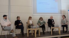 Sechs Personen sitzen auf dem Podium, Präsentationsfolie zeigt "Die Rolle der Kommunen auf dem Weg zur Nachhaltigkeit"