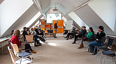 Workshopgruppe in hellem Dachgeschossraum, Referent steht vor Flipchart und Leinwand