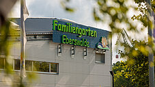 Gebäude des Familiengartens Eberswalde mit grünem Schriftzug, durch Blätter fotografiert