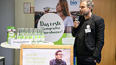 Person spricht ins Mikrofon vor Stand der PreussenquelleGmbH mit Mineralwasserflaschen