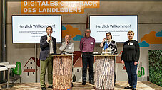 Fünf Personen stehen auf einer Bühne mit "Digitales Comeback des Landlebens"-Kulisse, zwei mit Mikrofon