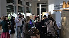Gruppe von Veranstaltungsteilnehmenden in einem Foyer in der Pause, rechts eine beschriftete Workshop-Tafel
