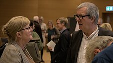 Zwei Personen stehen sich gegenüber und sprechen miteinander, weitere Personen im Hintergrund