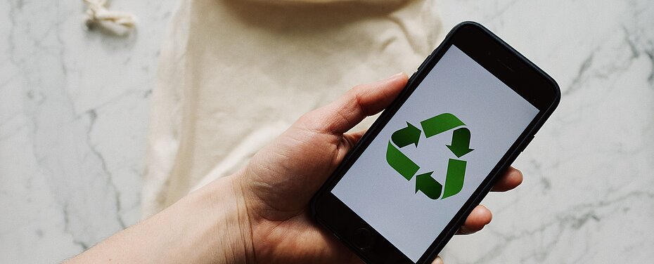Hand hält ein Handy in der Hand auf dem das Recycling-Symbol abgebildet ist.