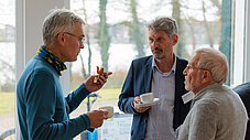 Drei Männer stehen zusammen und unterhalten sich beim Kaffee während einer Veranstaltungspause