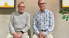 Zwei Personen sitzen nebeneinander vor dekorativer Wandgestaltung mit Pflanzen-Motiven