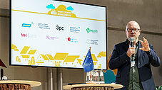 Person präsentiert mit Mikrofon vor Leinwand mit Smart Country Brandenburg-Logos und EU-Fahne