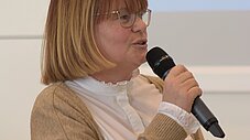 Person spricht sitzend ins Mikrofon, Präsentationsleinwand im Hintergrund