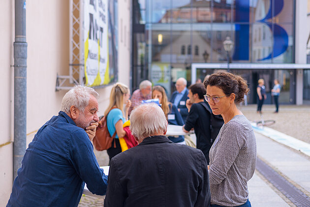 Kleine Gruppe von Personen im Gespräch im Freien vor einem Gebäudeeingang