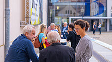 Kleine Gruppe von Personen im Gespräch im Freien vor einem Gebäudeeingang