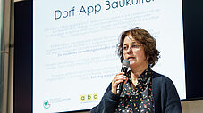 Person spricht ins Mikrofon vor Präsentationsfolie zur Dorf-App Baukultur
