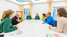 Gruppe sitzt an langem Tisch mit bunten Moderationskarten und arbeitet gemeinsam in einem Workshop