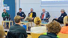 Podiumsdiskussion mit fünf Personen vor Publikum, einer spricht ins Mikrofon