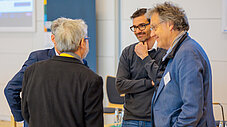 Drei Männer stehen zusammen und sprechen miteinander in einem Konferenzraum