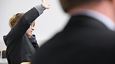 Person hebt die Hand im Seminarraum, um sich zu Wort zu melden