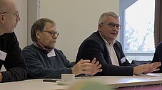 Drei Männer sitzen an einem Tisch und diskutieren in einer Workshopsituation