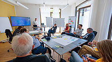 Gruppe arbeitet in einem hellen Workshopraum mit Flipcharts, Tischen und Bildschirm (Rechte: @RIFS und GFZ / Reinhardt & Sommer)