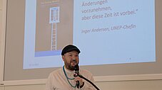 Person spricht am Rednerpult mit Mikrofon, Präsentationsfolie im Hintergrund zeigt Zitat von Inger Andersen, UNEP-Chefin
